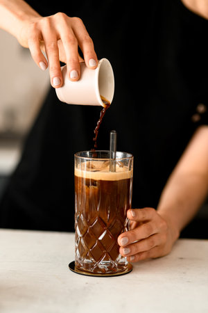 Barista woman pouring coffee on ice cubess in high old fashioned glass with tonic served on table in...