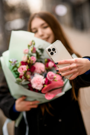 Young cheerful lady takes selfie holding delicate flower bouquet of eustoma, carnations, anthurium and eucalyptus wrapped in mint color paperの写真素材