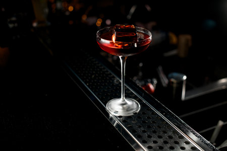 Autumn or winter red cocktail in high martini glass with ice cube on bar counter. Close up view. Dark blurred backgroundの写真素材