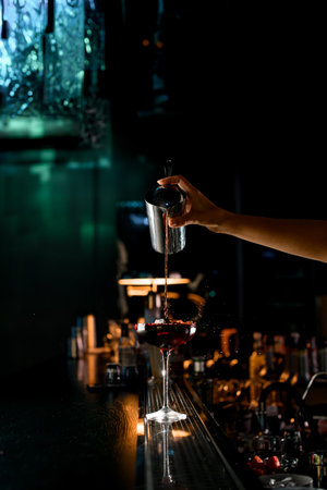 Great view of woman bartender pours liquid to crystal clear cocktail glass with ice cube. Making cocktails concept. Dark blurred backgroundの写真素材