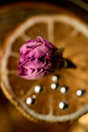 Selective focus on transparent yellow cocktail decorated with dried orange, silver beads and little rose flower, top view. Dark backgroundの写真素材