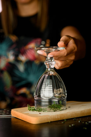 Female bartender covers burning greens with empty glass to keep the smoke inside at bar counter. Blurred background. Presentation drinks at barの写真素材