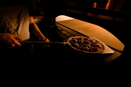 Chef puts pizza into oven with oven shovel for baking.の写真素材