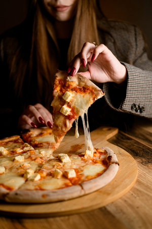 Delightful moment. Girl takes the first stretchy cheese pizza slice.
