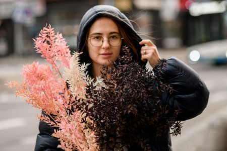 Dry bush and a pink bouquet in the hands of a cute girl standing on the street