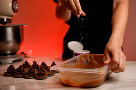 Confectioners female hands sprinkle chocolate cream in plastic container with coconut shavingsの写真素材