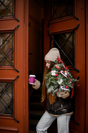 Standing near the door girl with a coffee in hand with a decorated fir branchesの写真素材