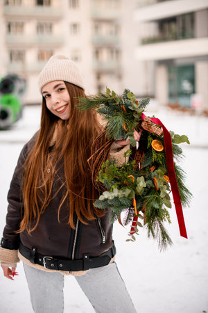 Dark hair girl with a smile in a beige hat with a bouquet of decorated fir branchesの写真素材