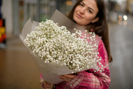 Young woman holding a bouquet of white small flowers in a transparent wrapper on a blurred backgroundの写真素材