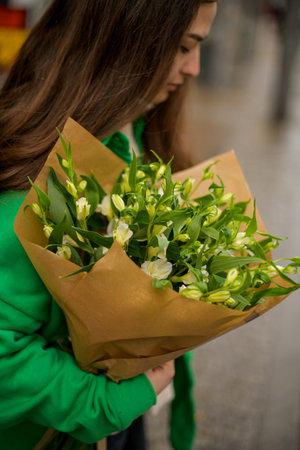 Woman in a green sweater holds a bouquet of alstroemeria in a paper brown wrapper