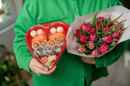 Female hands hold a bouquet of tulips and a heart shape with a sushiの写真素材