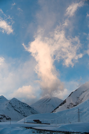 Under a blue sky with white clouds, a mountain massif covered with snow spreads out