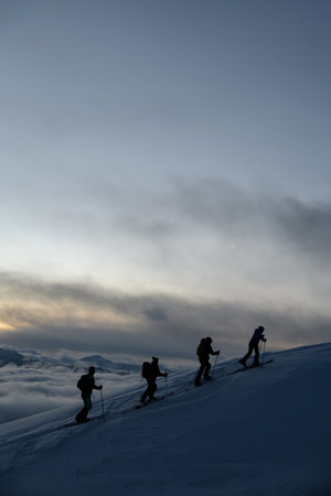 Silhouettes of four skiers with poles have almost reached the highest point of the mountain massifの写真素材