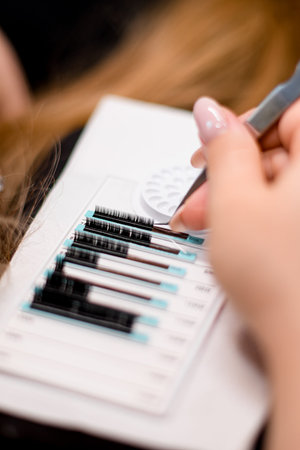 Female hands of a stylist takes artificial eyelashes with tweezers