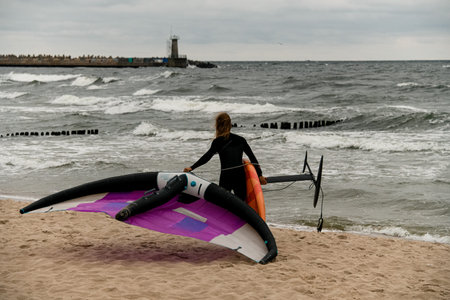 Young man walks along the seashore with a board and wings for wingfoiling