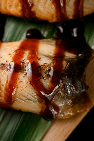 Rolls wrapped in salmon slices drizzled with sauce on a banana leaf close up