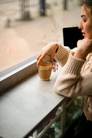 Young woman in a light beige jacket with a craft glass of coffee in her handsの写真素材