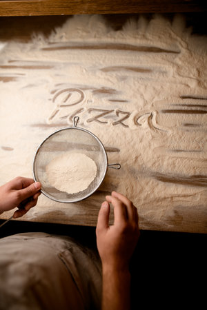 Letters made on flour sifted through a metal sieve on a textured wooden table before making pizzaの写真素材