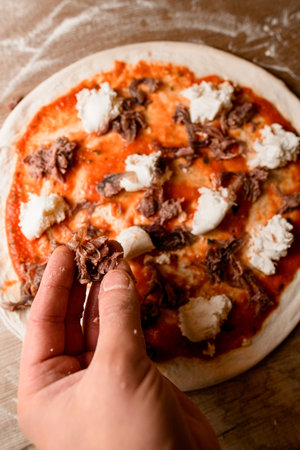 Hands make a pizza on a round pizza blank on a textured tableの写真素材