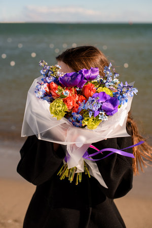 Stylish brunette woman in black coat hides by bright flower arragementの写真素材