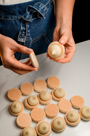 Female hands of a confectioner fasten halves of pink macaroonsの写真素材