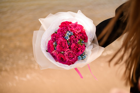 Bouquet of red and blue flowers in white paper on a background of blurred sandの写真素材