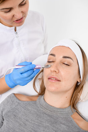 Cosmetologists hands perform the procedure of electroporation of the area under the eyes in a beauty...