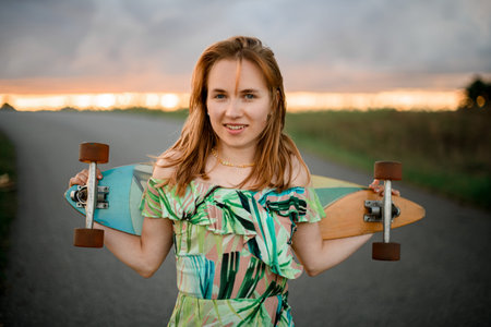 Young woman sincerely smiles and holds a longboard with her hands behind her back