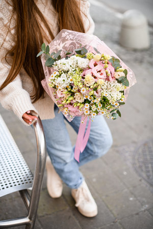 Unrecognizable girl with long hair holds in her hands delicate mix of eustoma flowers, daisies, eucalyptus wrapped in vintage package with pink ribbonの写真素材