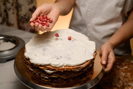 Baker holds dried strawberries in his hand near the cakeの写真素材