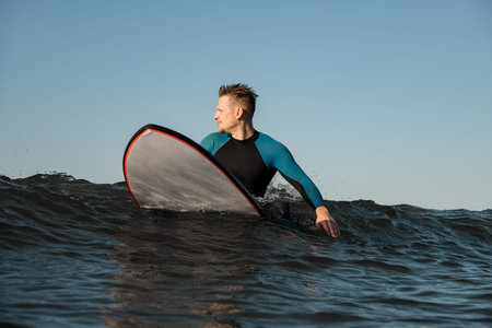 Serious handsome male surfer in the sea on a surfboard and looking into the distance waiting for a...