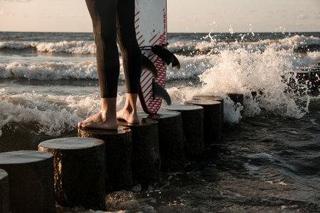 Male surfer legs in wetsuit standing on wooden stump near surfboardの写真素材