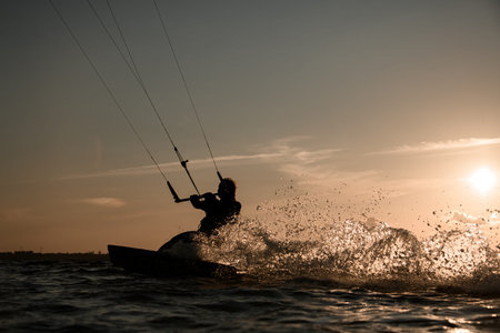 Female wakeboarder rides a wakeboard, holding on to a handle on a cable against the background of...