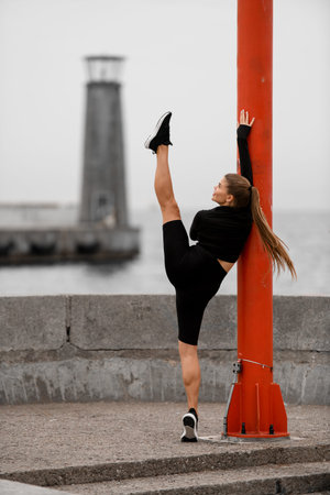 Cute fitness woman doing a toe-up stretch while standing with her back to the camera near a red...