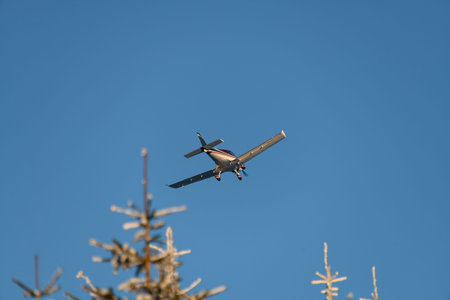 Beautiful view on sport aircraft flying over the snow covered evergreen fir trees
