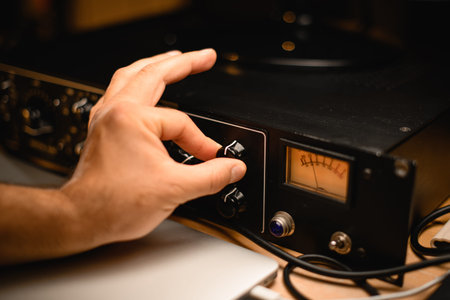 Close-up of a mans hand carefully turning a knob on a microphone preamplifier