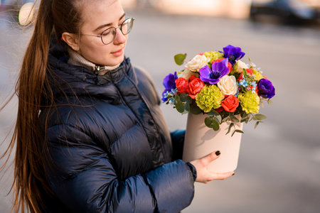 Young woman in glasses holds a delicate bouquet of colorful flowersの写真素材