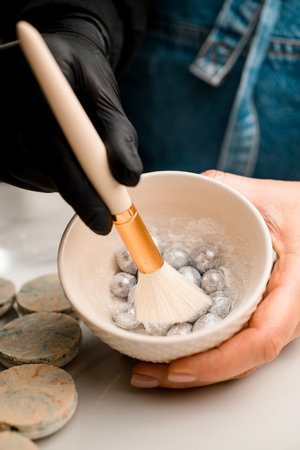 Womans hand holds a ceramic bowl with nuts sprinkled with silver paint, the other hand holds a brush