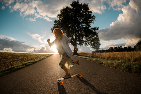 Sunlit cruise. Girl propels longboard forward, basking in sunshine.の写真素材