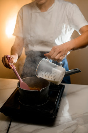 Chef in jeans makes cream for macarons on a black hot stoveの写真素材