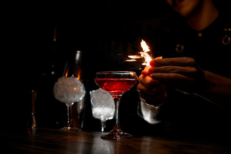 Bartender lighting a fire on the side of a cocktail glass in a cocktail glass on a tall stem