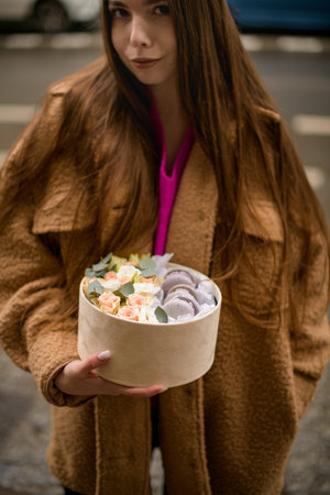 Charming girl hold in your hands a cardboard bouquet box with a macarons and flowers