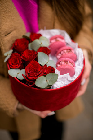 Pink macarons and red roses in cardboard box in hands of a girlの写真素材