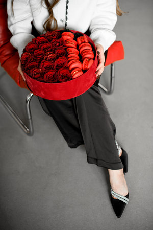Red gift box with red roses and red macaroons lies on the lap of a young womanの写真素材