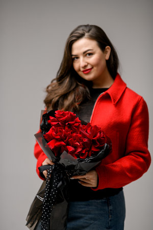 Young pretty woman in a red jacket holding a bouquet of red rosesの写真素材