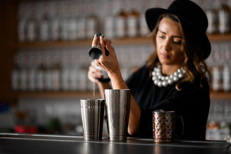 Female bartender pours a clear drink from a jigger into a shakerの写真素材