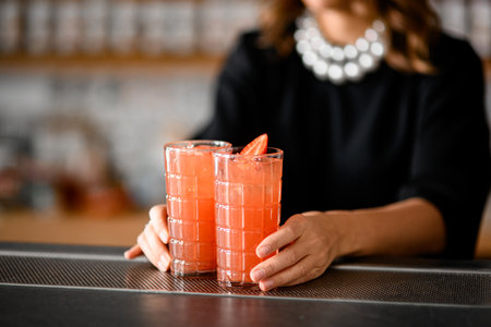 Female hands holding two glasses with pink cocktail with half of strawberryの写真素材