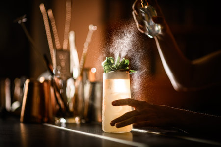 Female hands of bartender spraying cocktail decorated with leaves in glass
