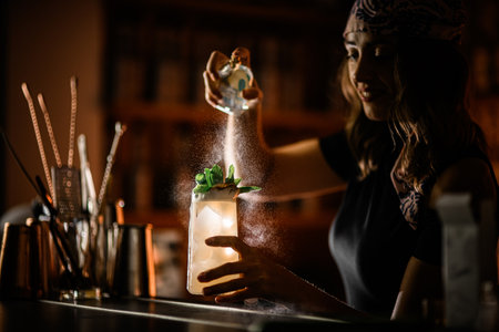 Happy pretty woman bartender spraying a glass with a cocktail covered with condensationの写真素材