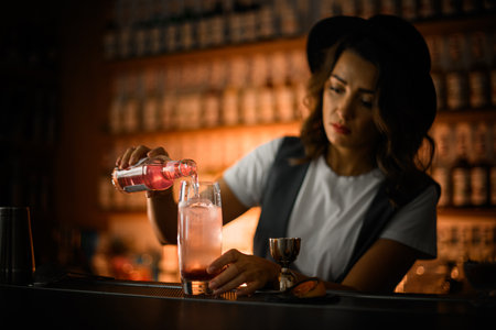 Female bartender is preparing a cocktail, pouring a pink drink from a bottle into a glass with iceの写真素材